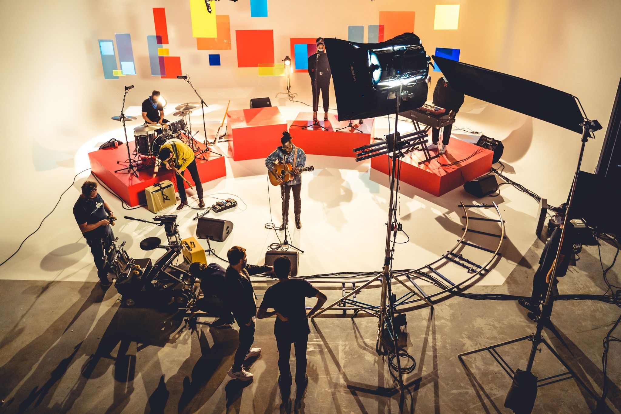 Looking down on a band playing a white set hung with colored squares, a curved dolly track and lights ringing the crew